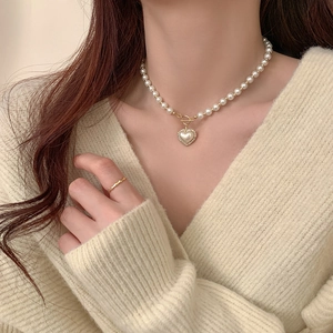 Detail of a pearl heart pendant necklace and wavy gold ring worn with a knit sweater