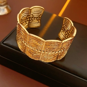 Detailansicht eines breiten goldenen Armreifs mit Wellenstruktur auf einer Lederbox