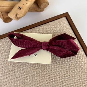 Macro detail of wine red velvet bow hair clip with textured corduroy fabric and metal grip