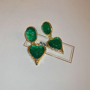 Close-up of vintage green resin heart earrings with gold pleated frames on a white box