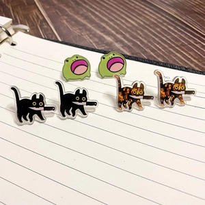 Detail of acrylic cat and frog earrings displayed on a white notebook page background