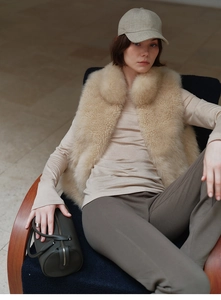 Detail of a beige faux fur vest styled with a handbag and casual earth-toned outfit