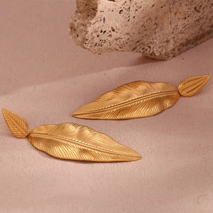 Macro view of detailed golden feather earrings with intricate leaf vein textures on stone