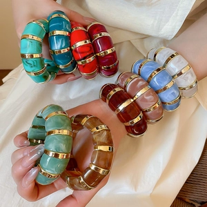 Detailed close-up of a colorful resin and gold metal link bracelet on a model's wrist
