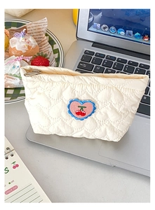Borsa trapuntata color crema con ricamo a cuore e ciliegia sopra un laptop argento
