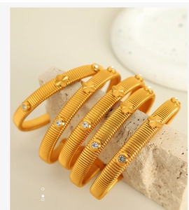 Detail of gold snake-bone bracelets with four-leaf clover design and zircons on stone