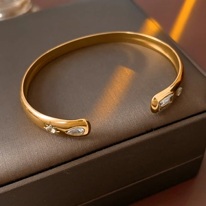 Detail of golden stainless steel bangle with teardrop zircon on a dark jewelry box