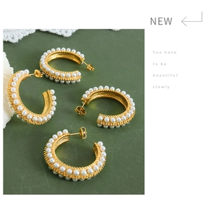 Close-up of C-shaped gold-plated earrings with double-row white pearls on green background