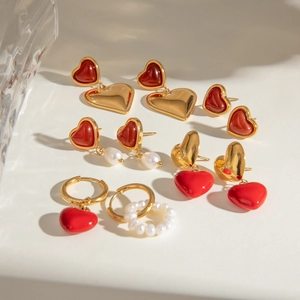 Gold stainless steel heart earrings with red resin and pearls on a neutral background