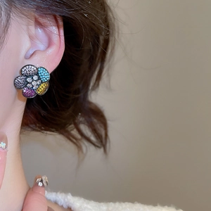 Macro view of colorful zircon flower earrings on ear with elegant stone textures