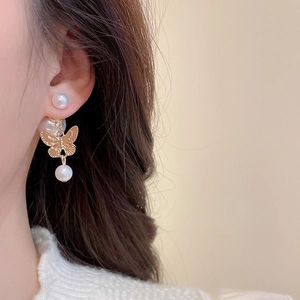 Detailed close-up of golden butterfly earrings with elegant white pearls on a model