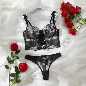 Detailed view of black floral lace bustier and matching thong set on white silk fabric
