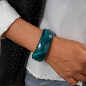 Detail of a wide dark green acrylic bangle with marble texture on a model's wrist