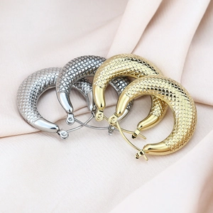 Textured gold and silver hoop earrings with fish scale pattern on pink silk background