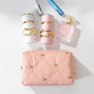 Flat lay of pink quilted makeup bag with bow embroidery and elegant perfume bottles