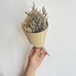 Mini dried flower bouquet wrapped in vintage newspaper paper held against white wall