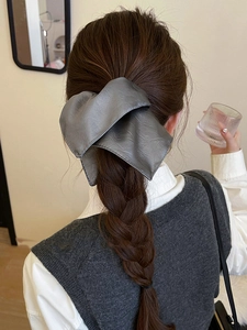 Detail of grey leather bow hair tie worn on a ponytail for a vintage fashion style