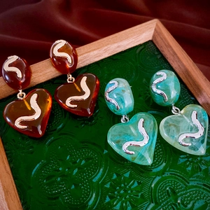 Close-up of amber red and mint green heart-shaped acrylic earrings on textured glass