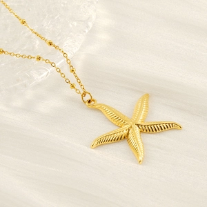 Gold starfish pendant necklace with beaded chain on a white textured background