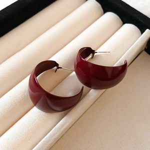 Detail view of glossy dark red C-shaped hoop earrings placed in a beige ribbed storage box