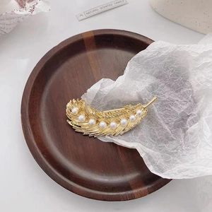 Detailed view of a golden feather hair clip with white pearls on artistic paper