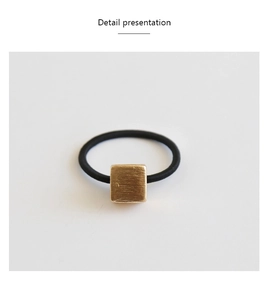 Detail of minimalist black hair tie featuring a brushed gold square metal accent piece