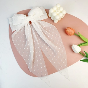 Detail of white Swiss dot chiffon bow hair clip with long ribbons on a pink display mat
