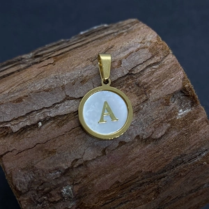 Golden round pendant with white mother-of-pearl shell and letter A on wooden background