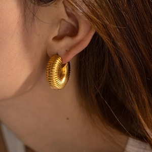 Detail of chunky gold hollow hoops with textured screw-thread design on model