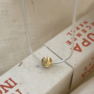 Macro shot of silver snake chain necklace featuring a brushed gold spherical bead charm