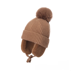 Detail of brown knit baby hat featuring fuzzy pompom and soft faux shearling earflap lining