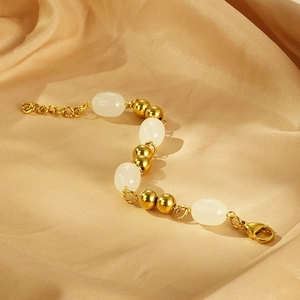Detail of gold beaded bracelet with white oval resin stones on luxury champagne silk fabric