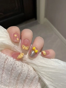 Detail of press-on nails with yellow bow, glitter, and star patterns in square-oval shape