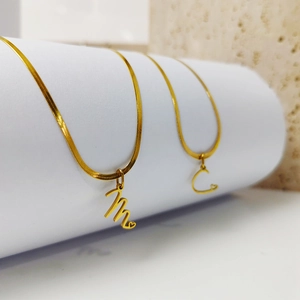 Close-up of gold stainless steel snake chain with cursive initial M and C pendants