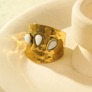 Macro shot of gold hammered wide ring with three white teardrop stones on a ceramic tray