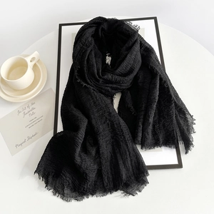 Detail of black wrinkled linen scarf featuring raw fringe edges and soft textile texture
