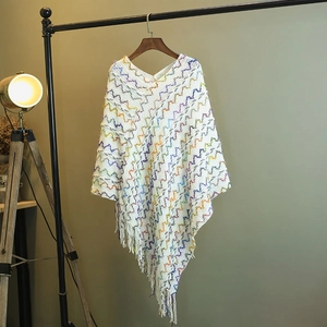 Détails du tricot d'un poncho bohème blanc avec motifs ondulés colorés et des franges