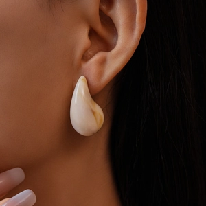Close-up of cream teardrop earring with brown marble pattern on model