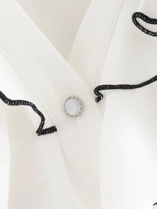 Close-up of cream ruffled blouse with black wavy trim and elegant pearl button detail