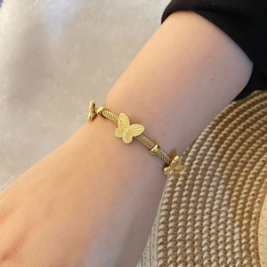 Gros plan d'un bracelet papillon doré avec maille tissée porté sur un poignet féminin