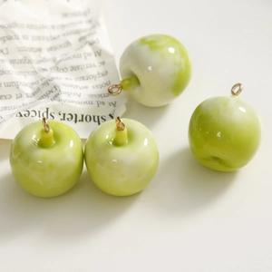Macro shot of four mini green resin apple charms with gold rings for DIY jewelry making