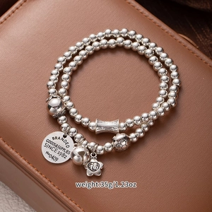 Close-up of multi-layer silver bead bracelet with lucky cat bell and flower pendants