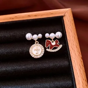 Asymmetric pearl earrings with golden coin cross pendant and red enamel rocking horse charms