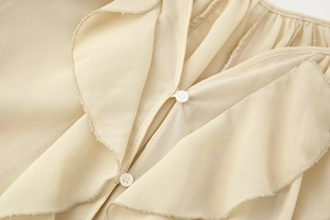 Detail view of layered ruffles and white buttons on a soft beige V-neck blouse fabric