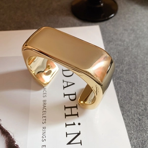 Close-up of wide polished gold metal cuff bracelet with reflective mirror finish surface