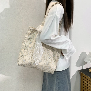 Floral canvas tote bag with lace bow detail shown on shoulder against a white wall