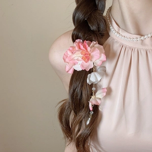 Détail d'une pince à cheveux fleur en mousseline rose avec de fins pompons sur tresse