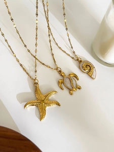 Macro shot of gold starfish turtle and conch pendants with white enamel on necklaces