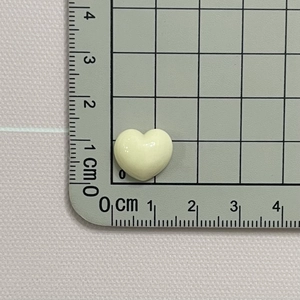 Close-up of a 1.2cm x 1cm glossy macaron beige resin heart charm on a scale
