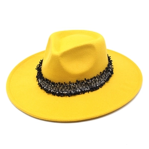 Détail d'un chapeau fedora jaune en laine avec bande à pompons noirs et blancs